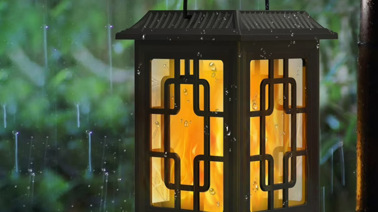Glowing, fire-lit lanterns lining a romantic walkway with stones and shrubs at night
