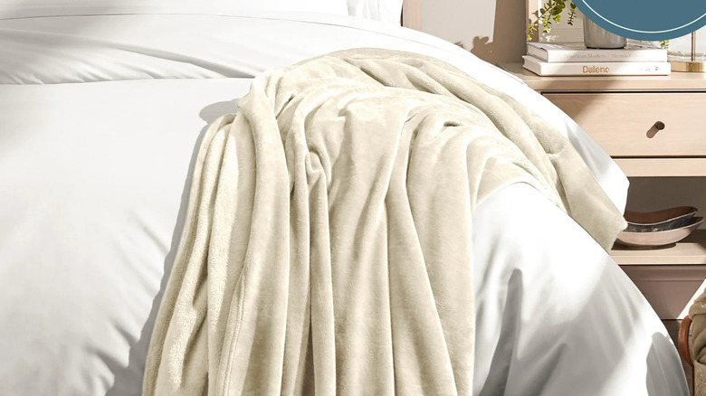 A cream Bare Home Microplush Fleece Blanket is draped on the end of a bed