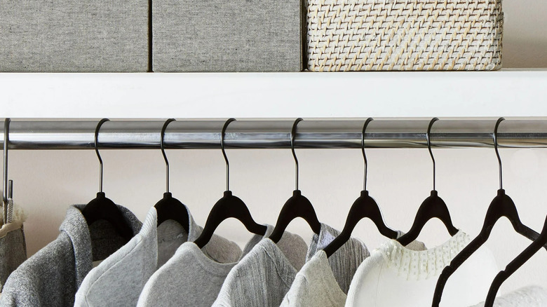 Black non-slip velvet clothes hangers hold neutral shirts hanging on a chrome closet rod