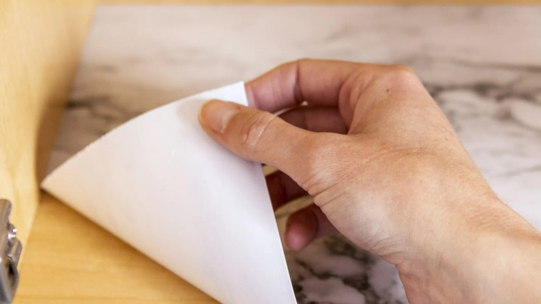 A person's hand lays a piece of marble-look EasyLiner Brand Contact Paper on a wooden shelf