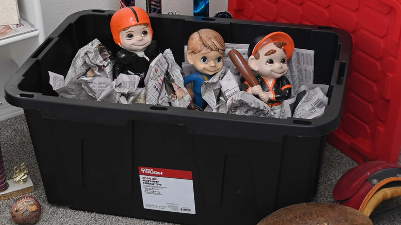 Three football figurines are surrounded by crumpled newspaper in a black Hyper Tough Large Storage Bin
