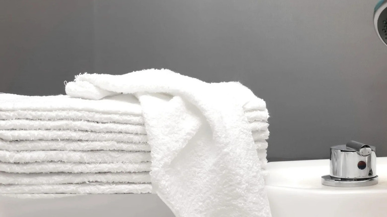 A pile of white washcloths is stacked on the edge of a white tub