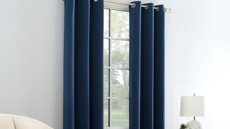 Navy blue blackout curtains hang on a window flanked by a cream armchair and metal side table