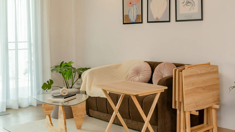 A neutral tray table sits in front of a brown couch in a neutral living room
