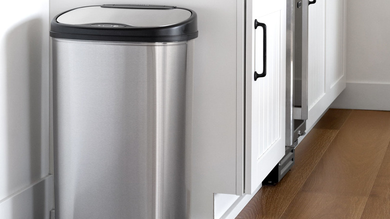 A Nine Stars Motion Sensor Automatic Kitchen Trash Can sits next to a row of white cabinets