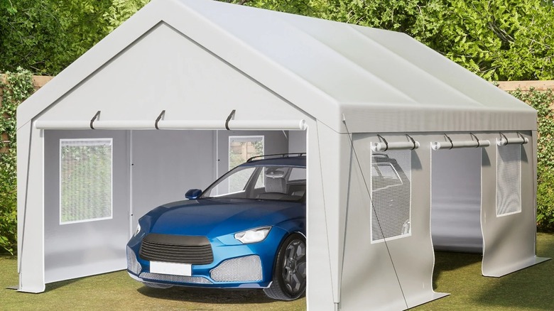 A blue car parked underneath a portable carport in a backyard.