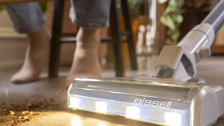 A Bissell PowerClean Self-Standing Cordless Stick Vacuum is lights up dirt covered tile floor