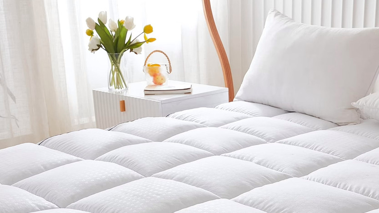 A thick white JUSTLET mattress topper lays on a bed in a calm white bedroom