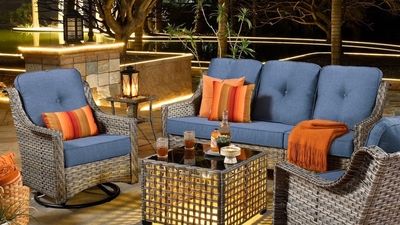 A five piece wicker patio set is neatly arranged on a stone patio