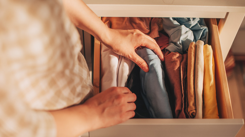 Person putting away neatly folded clothes in a dresser