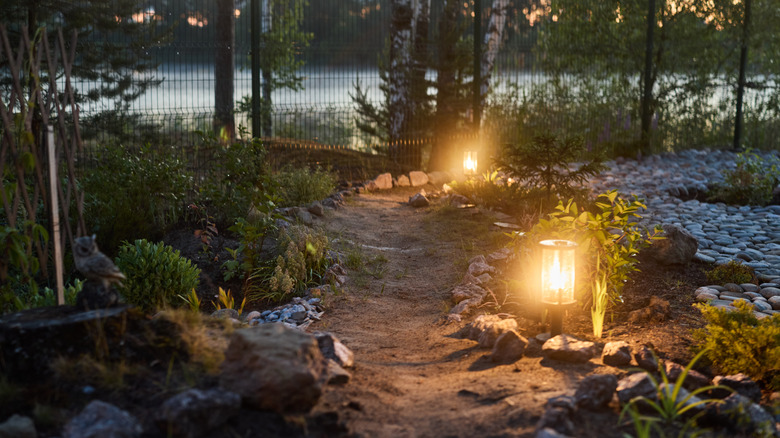 Glowing, fire-lit lanterns lining a romantic walkway with stones and shrubs at night