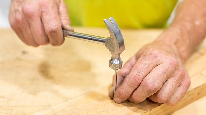 Man using Hyper Tough hammer to drive a nail into a piece of wood