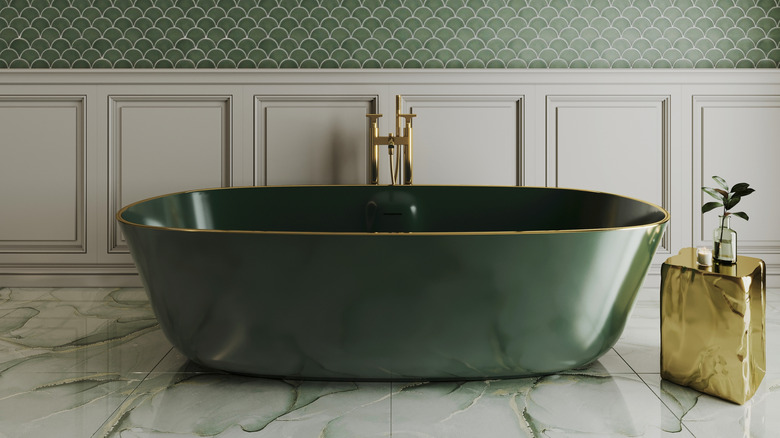 Modern luxury bathroom interior with a dark green freestanding bathtub, gold fixtures, and elegant fish scale tile wall.