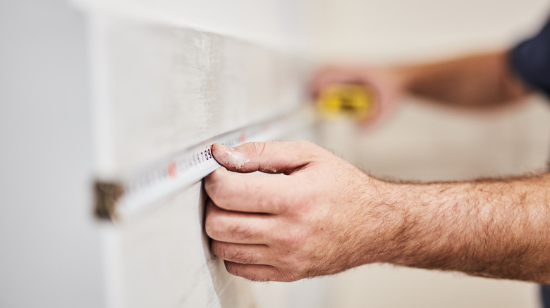 Hands using a measuring tape to measure a wall
