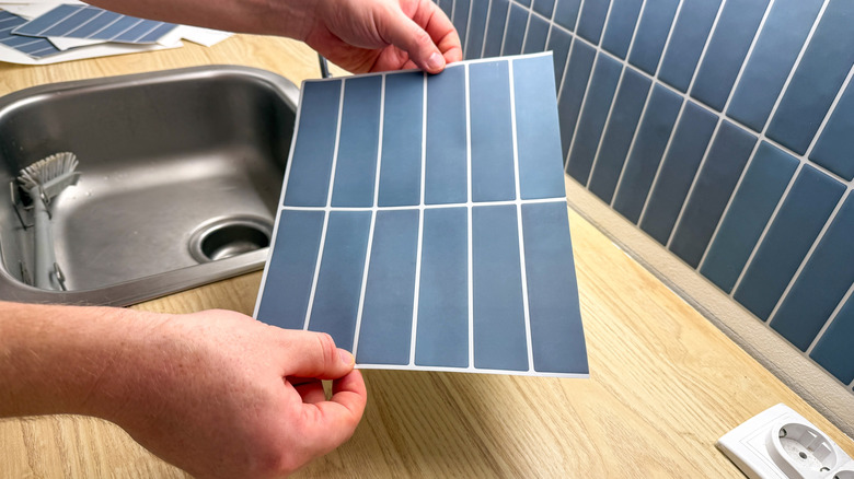 Man's hand holding a blue tile sticker