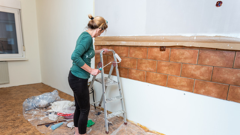 Woman preparing to paint a brown tile wall
