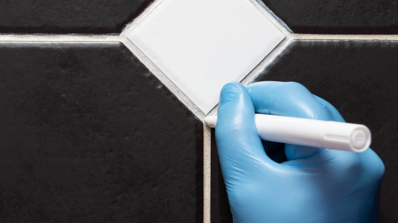 Blue gloved hand refreshing grout with a grout pen