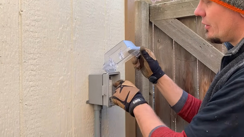 a man looks at an outlet box on the outside of a shed