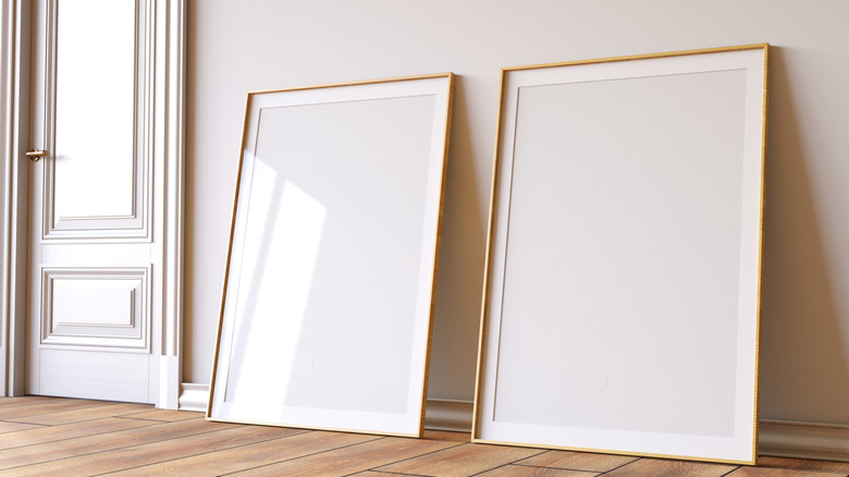 Two giant empty art frames lean against a blank wall.