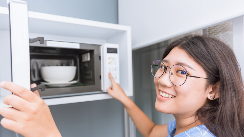Girl with glasses putting food in a microwave
