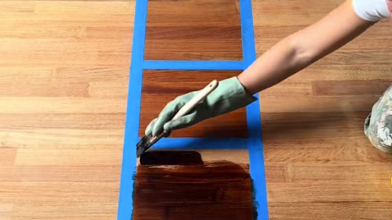 Hand painting stain on a sanded wood floor testing styles in small taped off sections