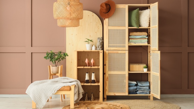 A wooden armoire with linens and a wooden shelf with shoes in front of a brown wall