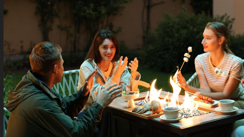 A group of people sitting around the BALI OUTDOORS fire pit, eating and talking