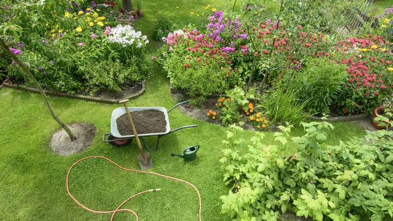 An aerial view of a flourishing garden with a wheelbarrow full of compost next to a spade and a watering can