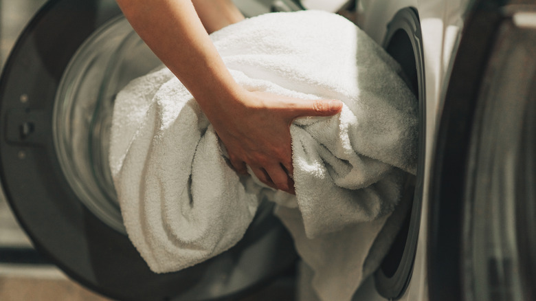 Arms loading white towel into washing machine