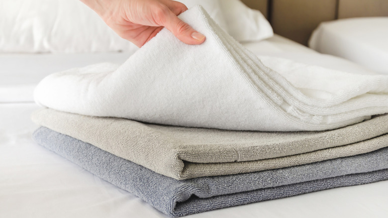 Hands placing neutral-colored towels onto a white bed