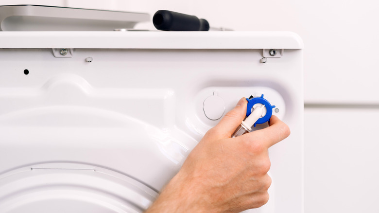 A person's hand tightening a hose on the back of a washing machine