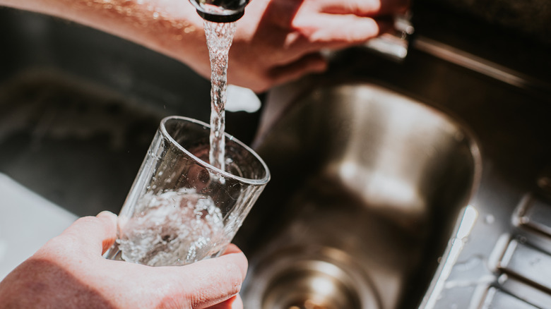 Hands holding cup and pouring faucet water into glass
