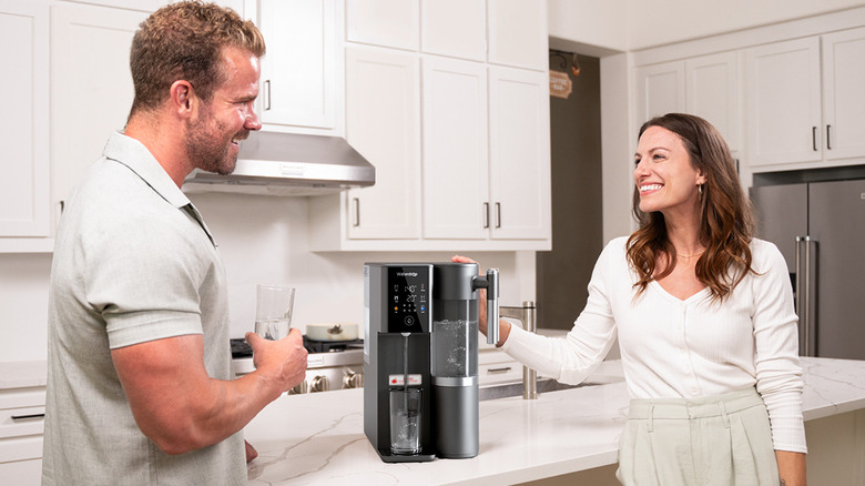 A smiling couple standing in the kitchen next to a water dispenser