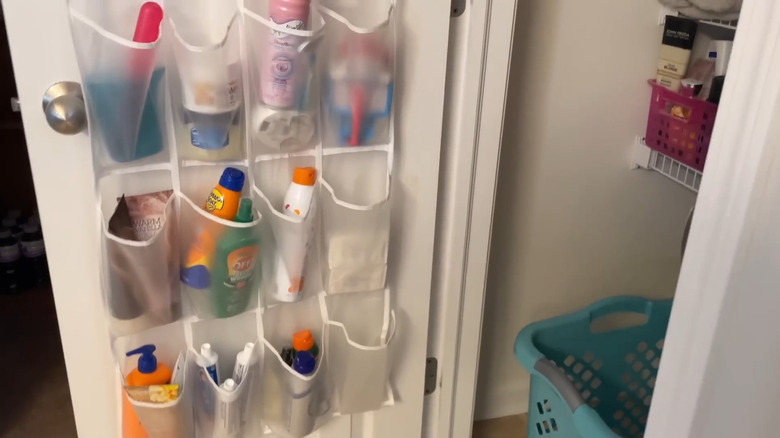 Assorted personal care items organized in the pouches of a shoe holder hanging on a linen closet door
