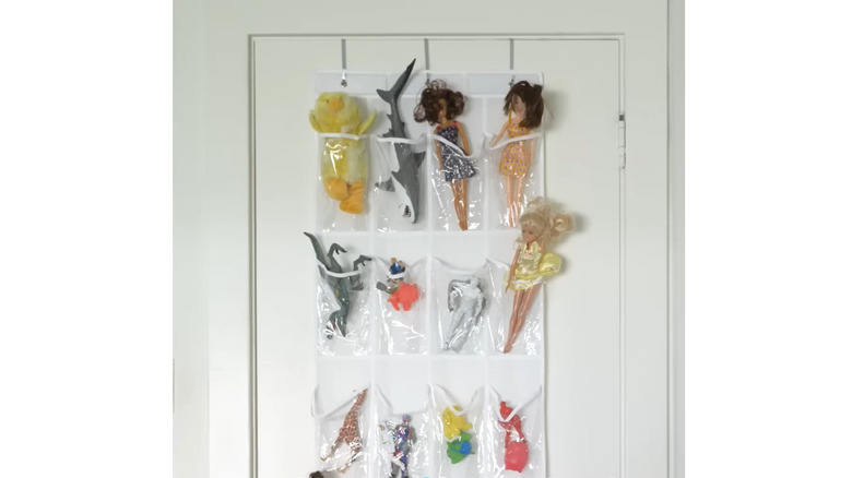Small plastic toys, figures, and dolls placed in clear plastic pouches on a shoe storage container hanging on a white door