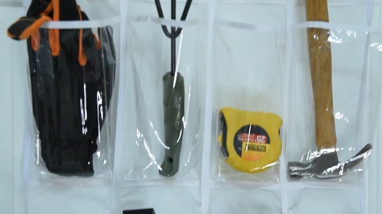 Work gloves, garden tools, tape measure, hammer, and other tools in a shoe organizer in the garage