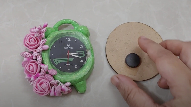 A crafter turns a small alarm clock face into a fridge magnet using air dry clay and a magnetised cardboard backing.