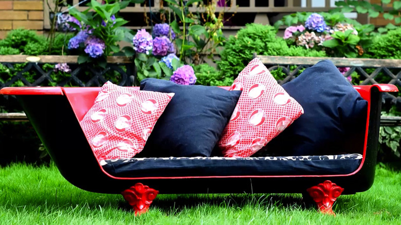 Red and black claw foot bath tub bench with navy blue and red throw pillows in a garden