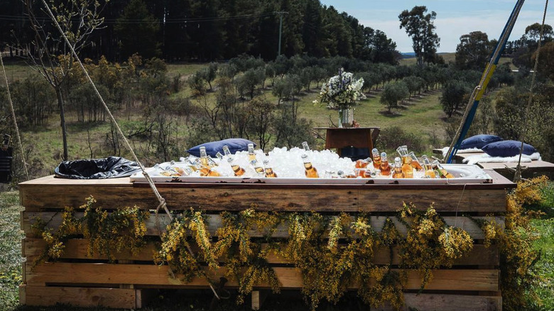 converted bathtub with a wooden frame containing ice and drinks in front of an orchard