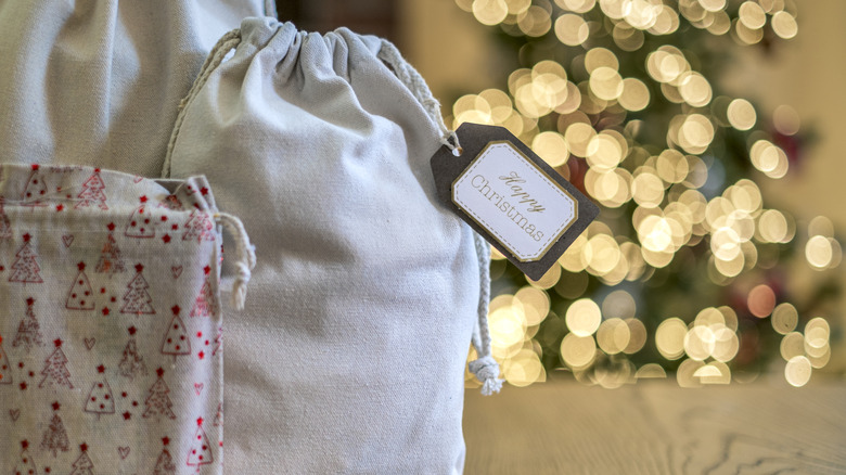 Fabric drawstring gift bags sit in the foreground of a blurry Christmas tree.