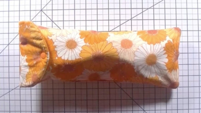 A yellow floral fabric pouch with snap closure sits on a drafting table with grid lines.