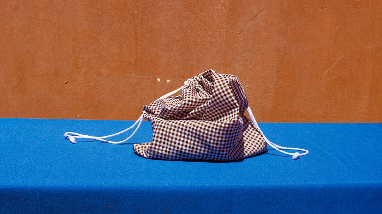 A red and white checkered drawstring bag sits on a bright blue tablecloth in front of a bright orange wall.