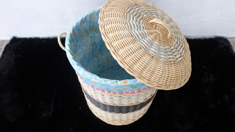 A wicker laundry hamper with blue patterned lining sit on a table covered with a black shag fabric.