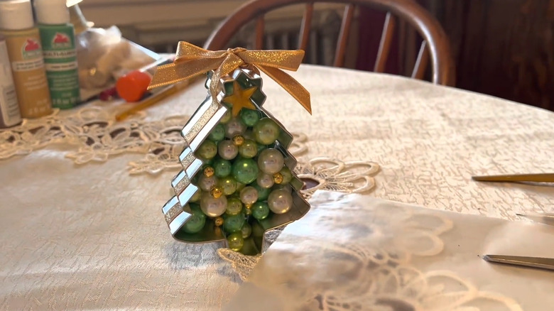 Metal Christmas tree cookie cutter filled with gemstones and wrapped in gold ribbon as an ornament