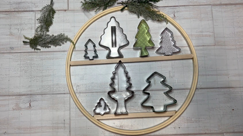Embroidery hoop with assorted Christmas Tree cookie cutters attached to mini shelves