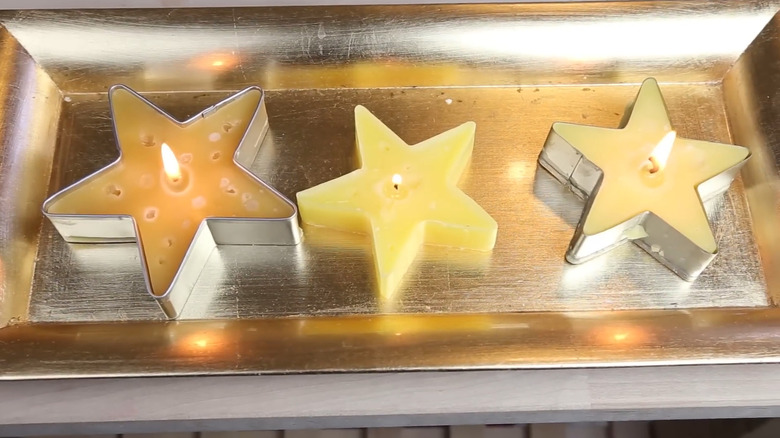 Three star-shaped candles burning on a tray and made using cookie cutters as the molds