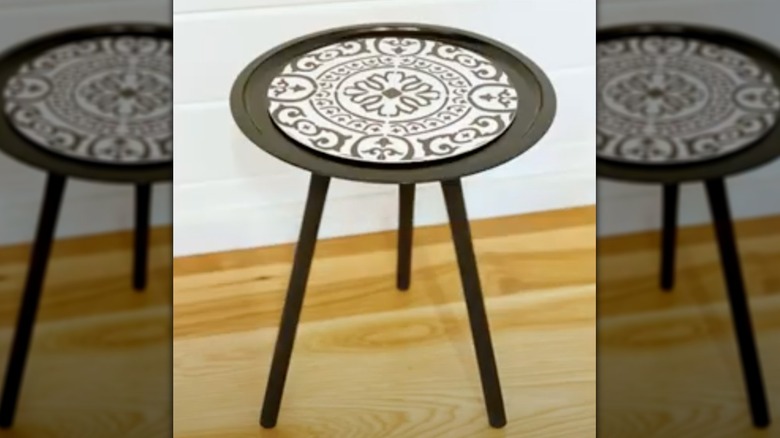 A black three-legged side table has a decorative black and white round on the top.