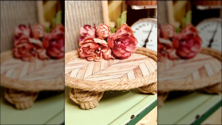An imitation wooden tray with rope border holds pink flowers.