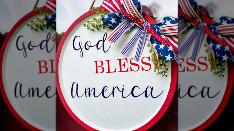 A white wreath says "God Bless America" and has a patriotic bow at the top.