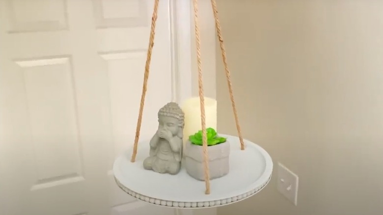 a white, beaded tray hangs holds decorative objects as it hangs from the ceiling.